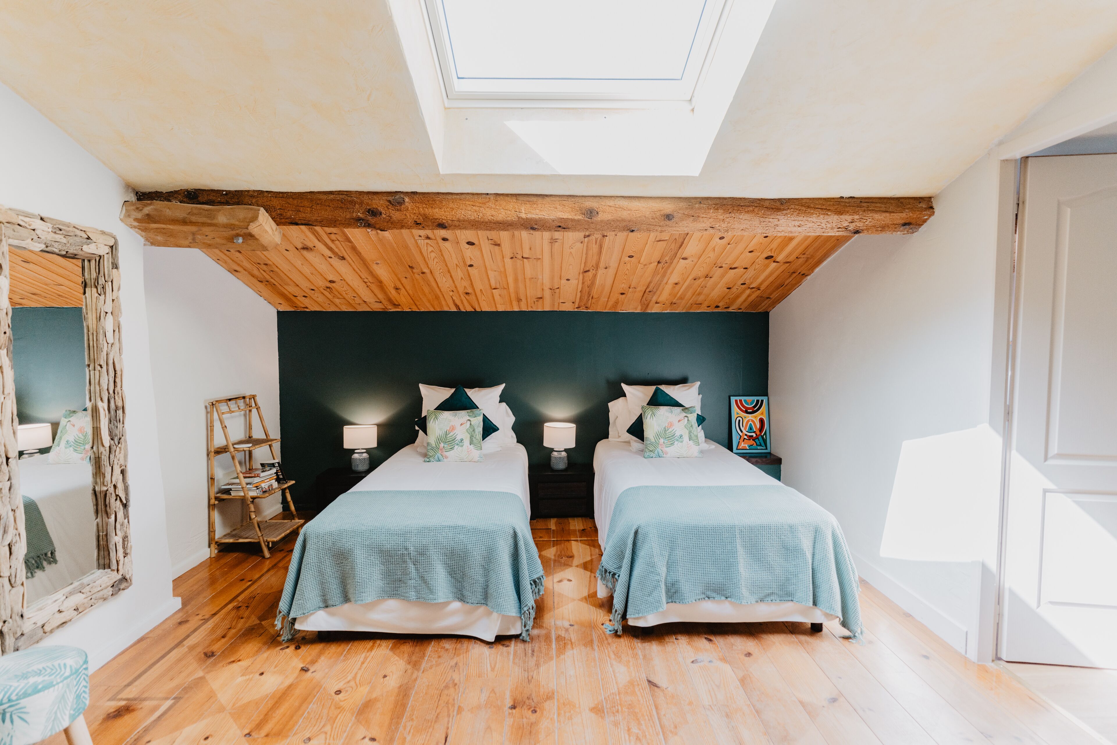 Un dormitorio con dos camas, vigas de techo de madera, un tragaluz y un espejo con marco decorativo.