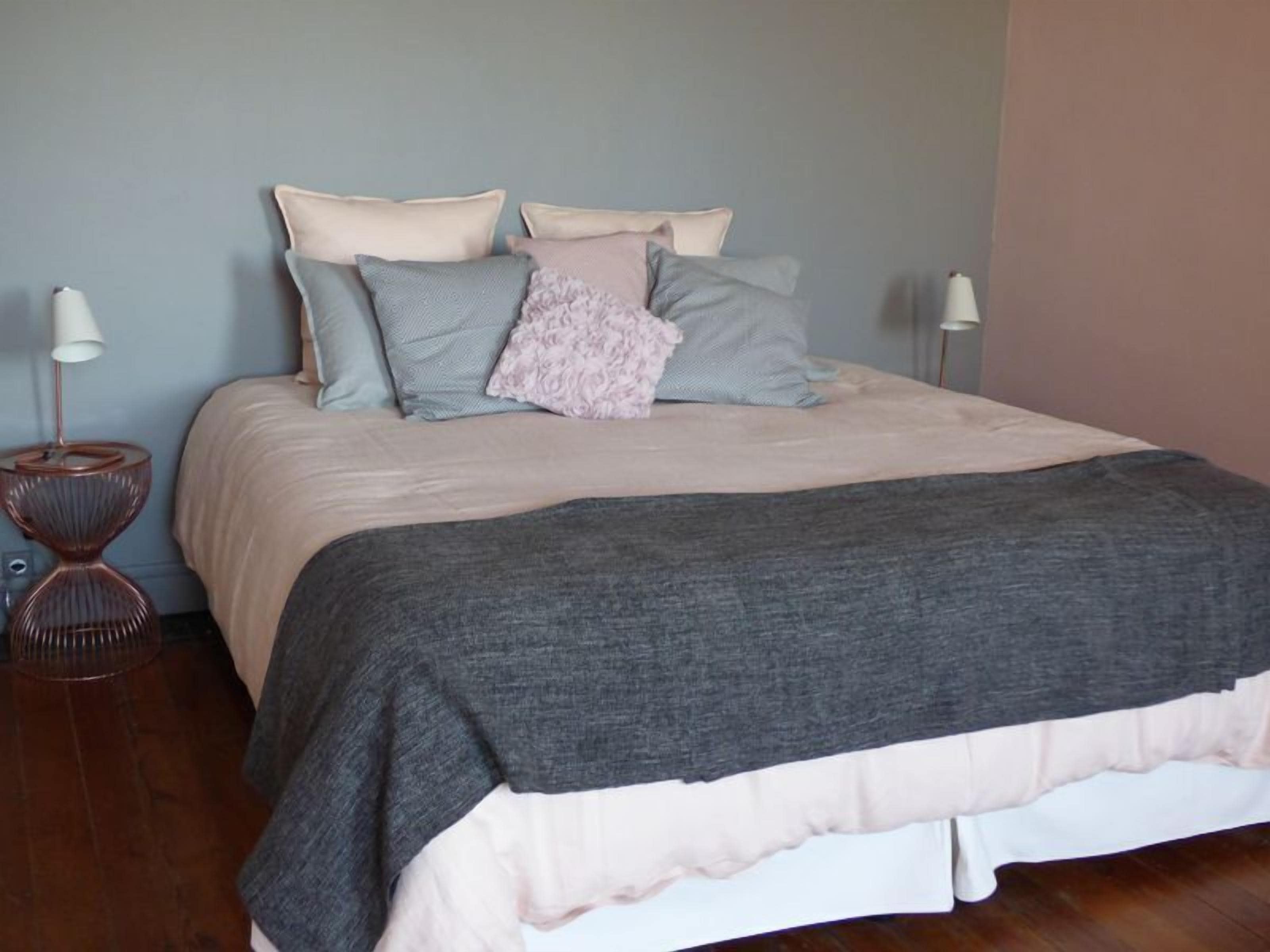 Una cama bien hecha con un edredón gris y varias almohadas de distintos colores.