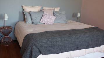 Una cama bien hecha con un edredón gris y varias almohadas de distintos colores.