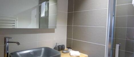 Un baño moderno con un lavamanos rectangular grande, un espejo encima y una zona de ducha con puerta de cristal.
