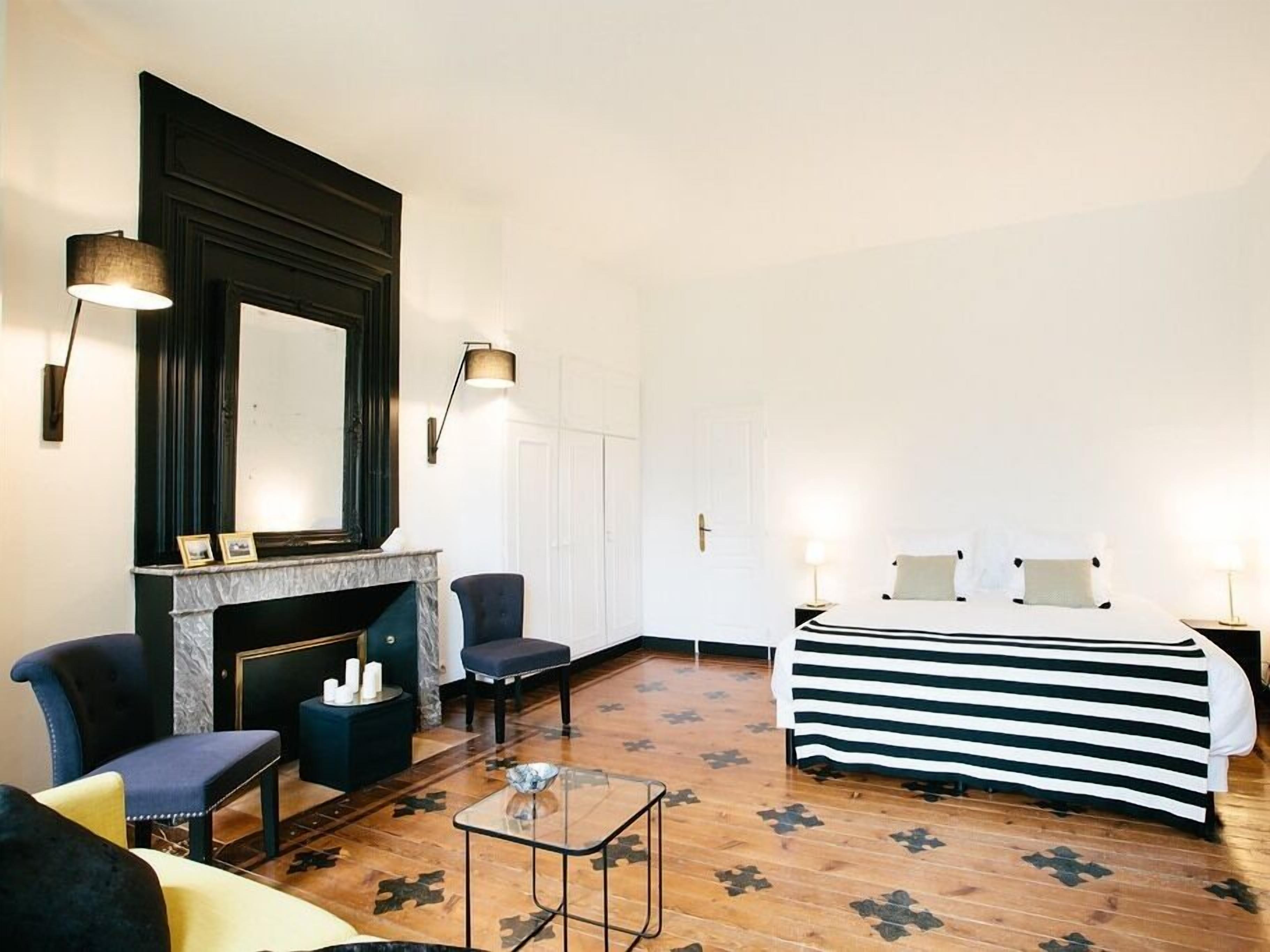 A hotel room with a fireplace, a bed with striped bedding, a small table, and two chairs.