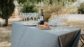 Une table à manger installée à l’extérieur, avec des assiettes, des verres et une bouteille de vin, le tout entouré de verdure.