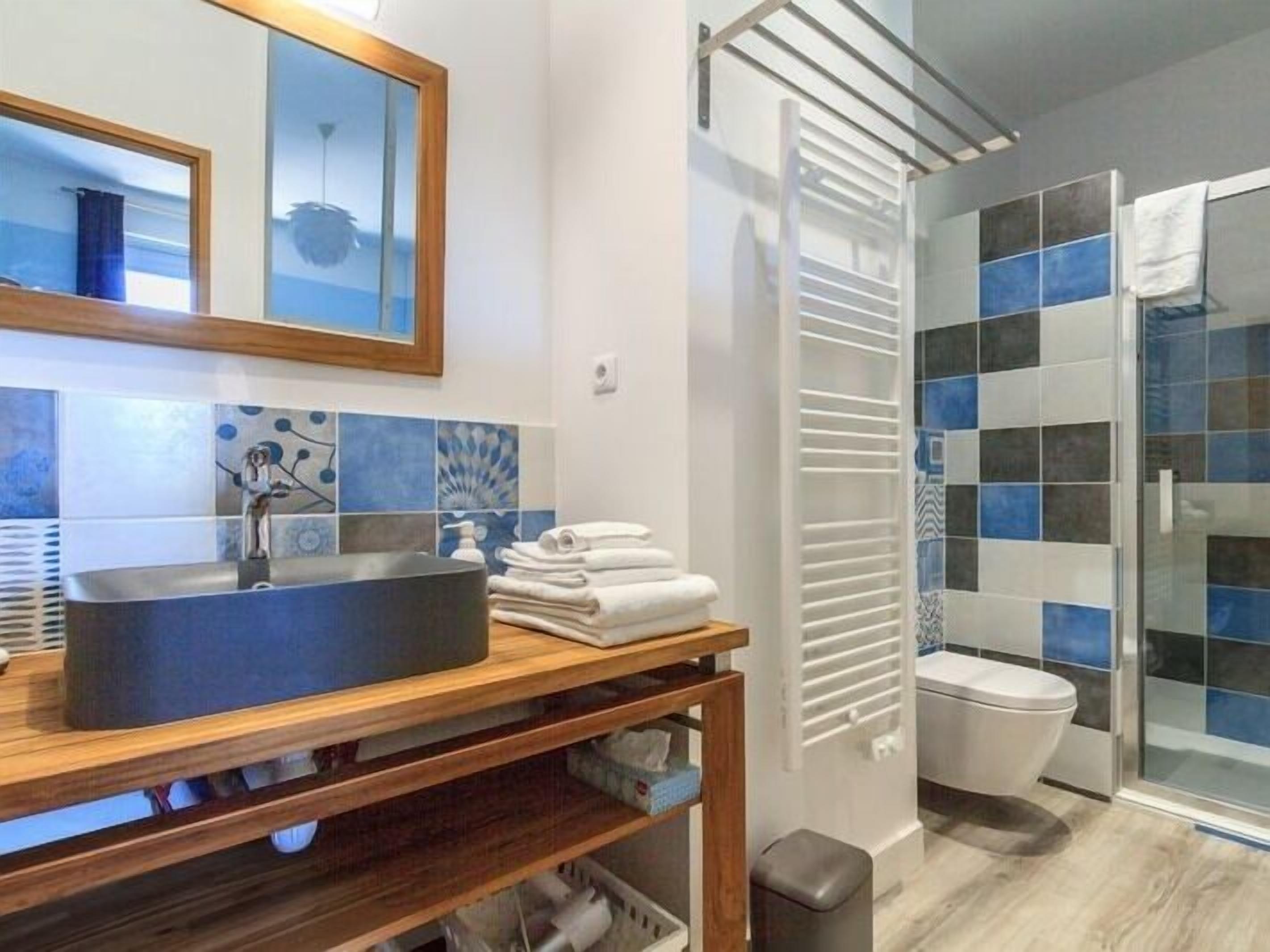 Un bany modern amb un mirall gran, un lavabo negre, un vàter i una zona de dutxa amb porta de vidre.