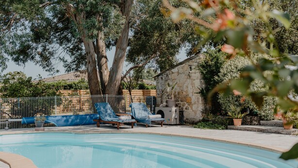 A swimming pool with lounge chairs, surrounded by trees and a stone wall. - Le Coeur des Vignes (Pauillac)