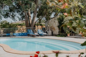 A swimming pool with lounge chairs, surrounded by trees and a stone wall. - Le Coeur des Vignes (Pauillac)