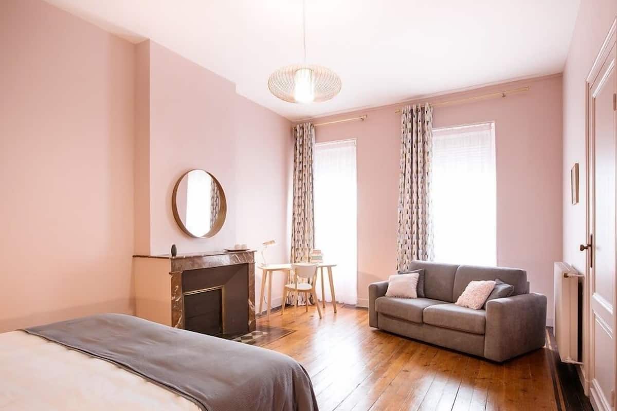 A bedroom with a bed, a sofa, a small table, a mirror, and a fireplace.