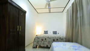 A bedroom with a bed, a wardrobe, a ceiling fan, and a window with curtains. - Villa ok (Unawatuna)