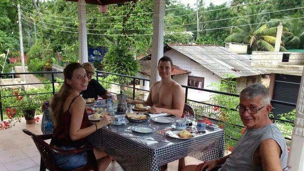 A group of people dining at an outdoor table with a checkered tablecloth, surrounded by greenery and a house in the background. - Villa ok (Unawatuna)