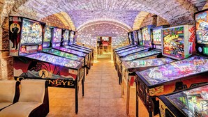 Una hilera de máquinas de pinball en una sala de juegos con paredes de ladrillo y un pasillo central.