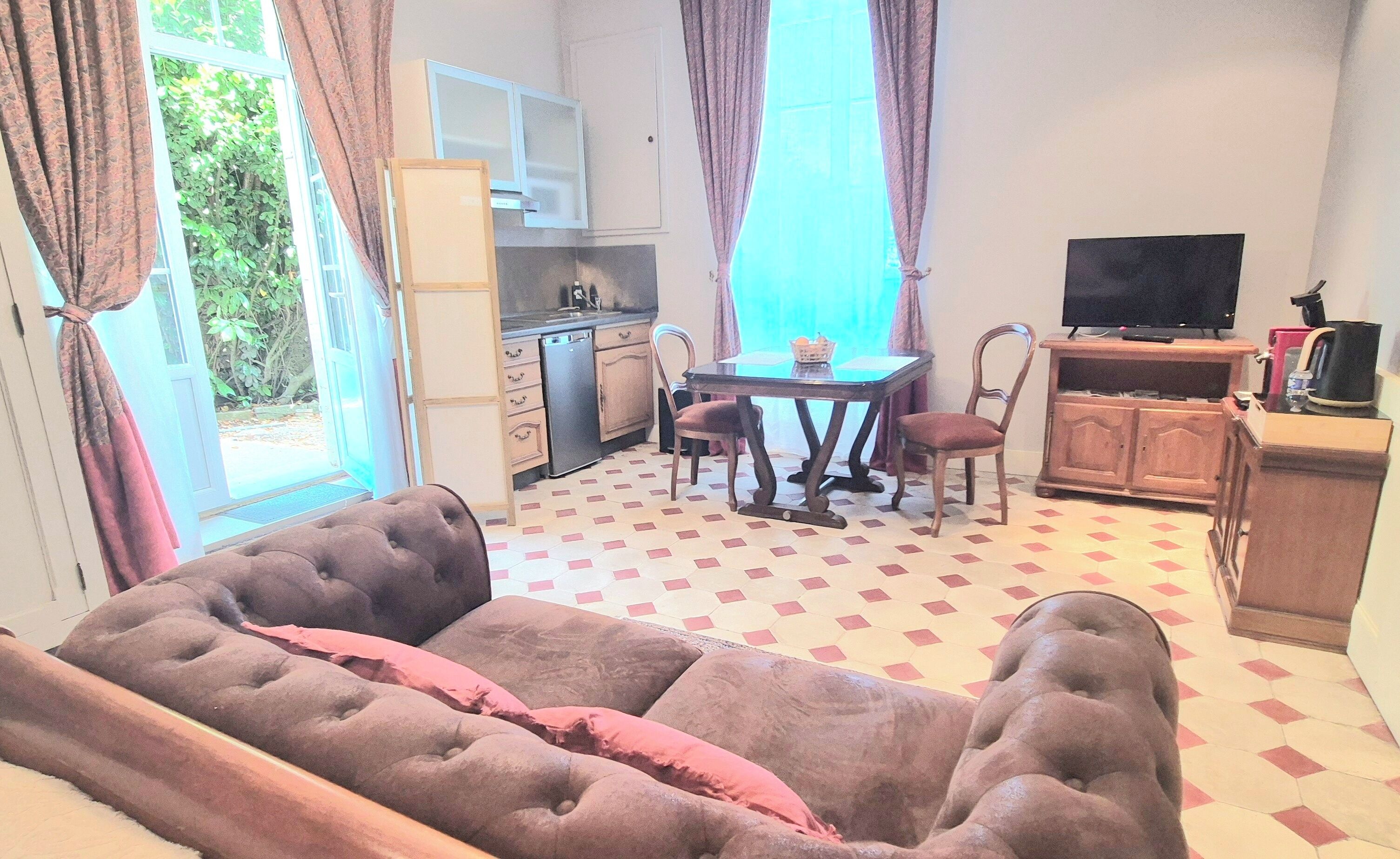 A living room with a sofa, a dining table with chairs, a television, and a kitchen area.
