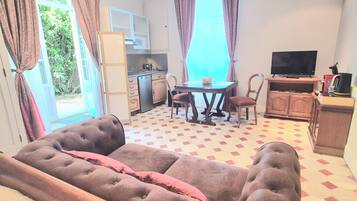A living room with a sofa, a dining table with chairs, a television, and a kitchen area.