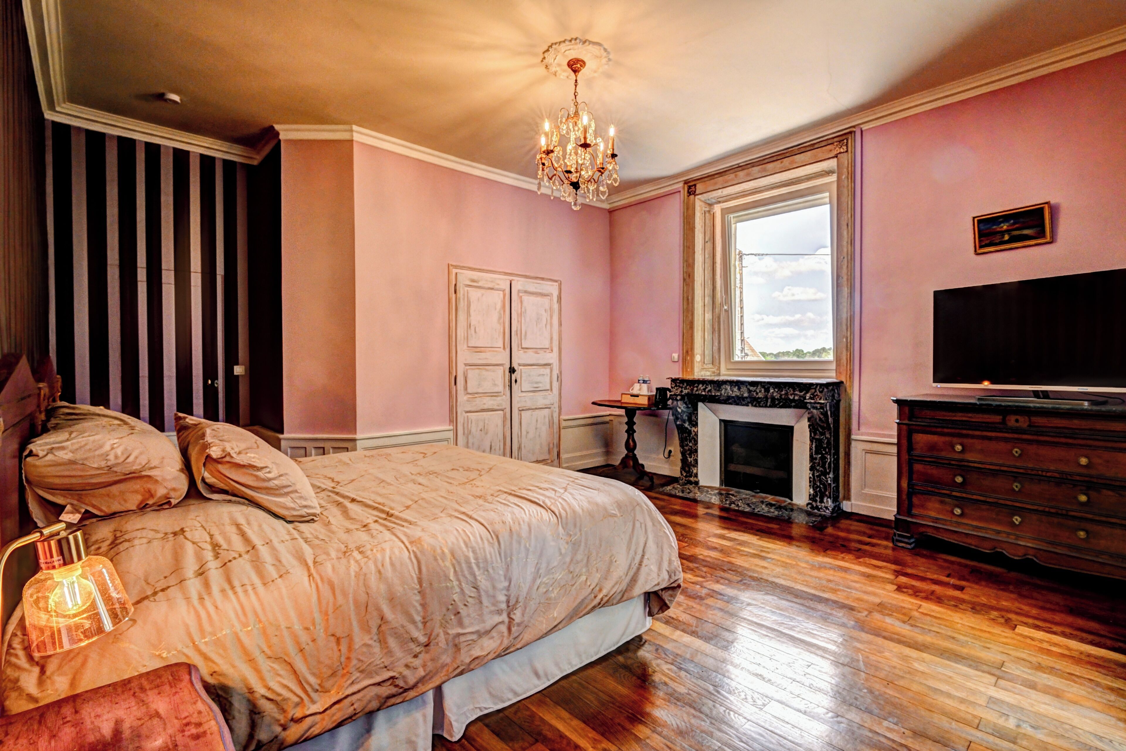 A bedroom with a large bed, a chandelier, a fireplace, and a television.