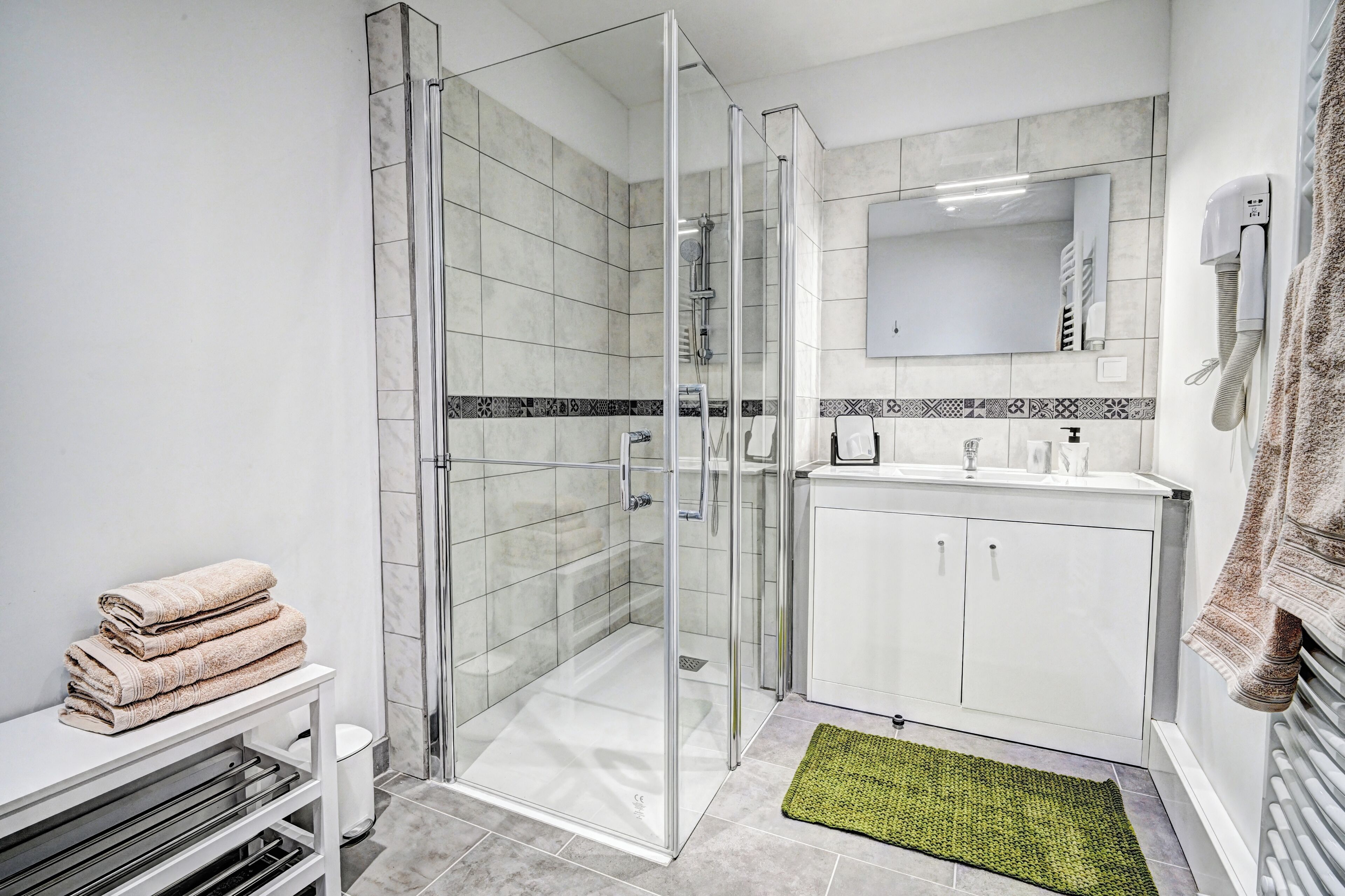 A modern bathroom with a glass-enclosed shower, white cabinets, a sink, and a mirror.