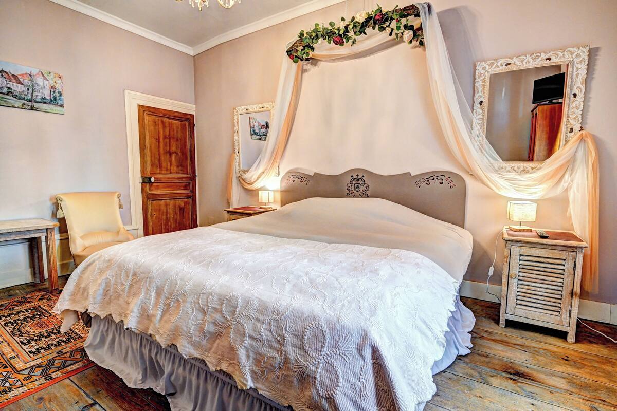 Une chambre à coucher avec un grand lit, une table de chevet en bois, une chaise, un miroir et une porte.