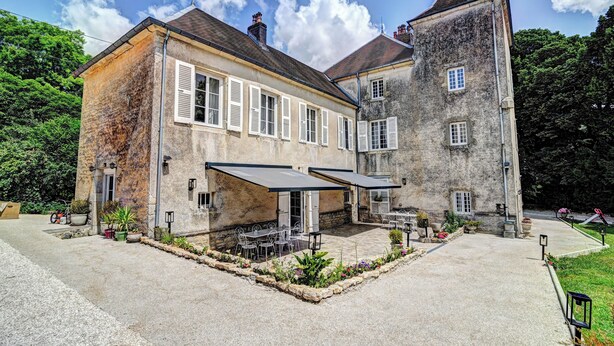 Un edificio histórico con patio, mesas al aire libre y una combinación de muros de piedra y enlucido.