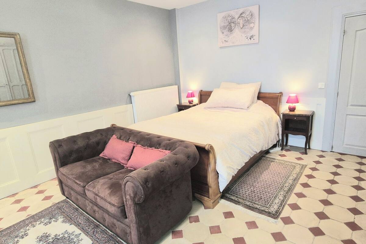 Une chambre à coucher comprenant un lit, une chaise, une table de chevet, une porte et un radiateur.