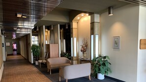 Eine Hotellobby mit Terrazzoboden, einer Sitzecke mit einer Couch und Sesseln, einer Zimmerpflanze und einem an der Wand befestigten Schild.
