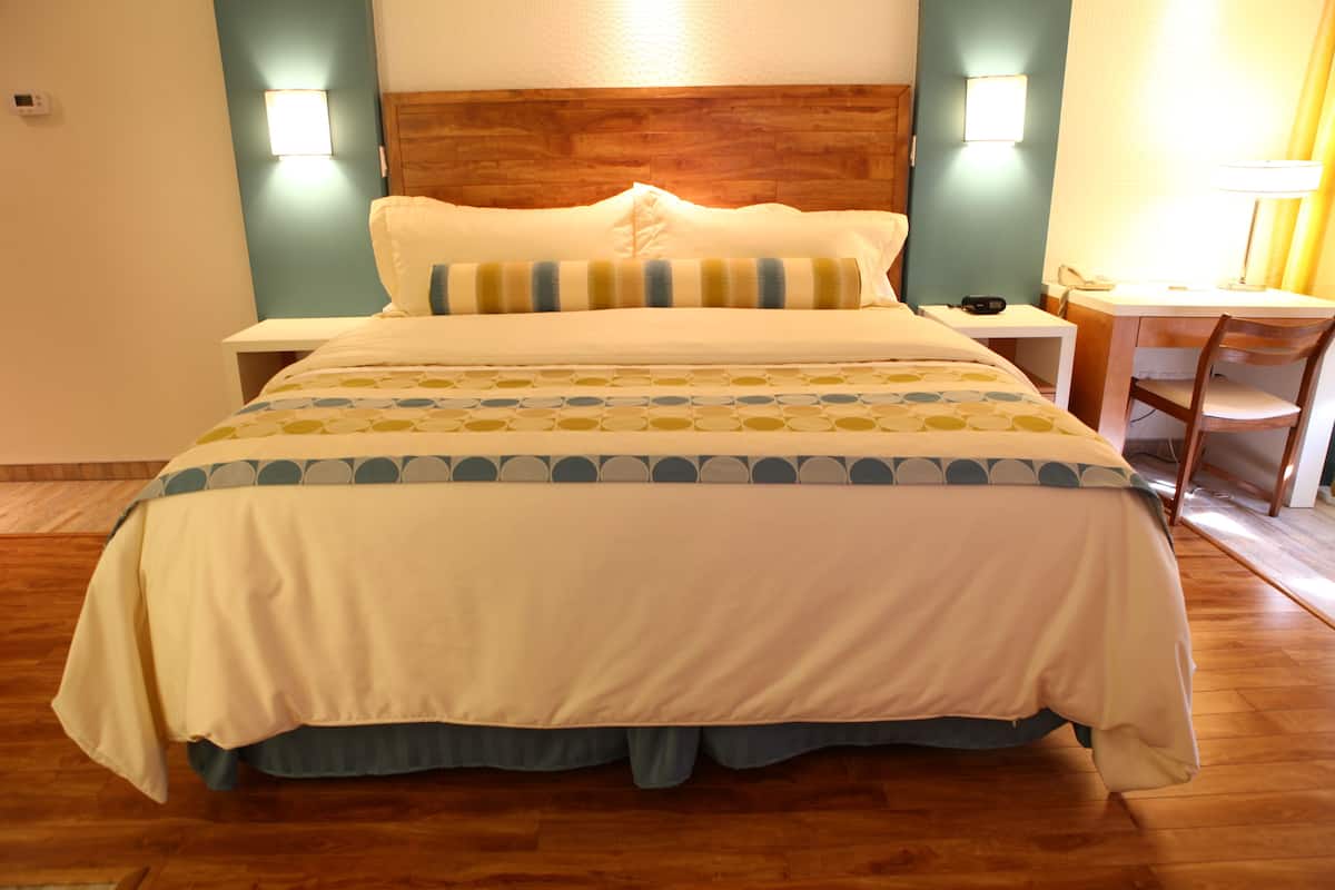 A hotel room with a wooden headboard, a bed with a patterned bedspread, bedside tables with lamps, and a desk with a chair.