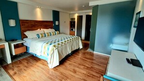 Ein modernes Hotelzimmer mit Holzboden, einem Bett mit gemustertem Überwurf, einem Schreibtisch mit Telefon und einem Fernseher.