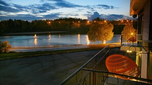 Ein Balkon mit Blick auf einen Fluss im Abendlicht, ein Baum und ein Geländer.