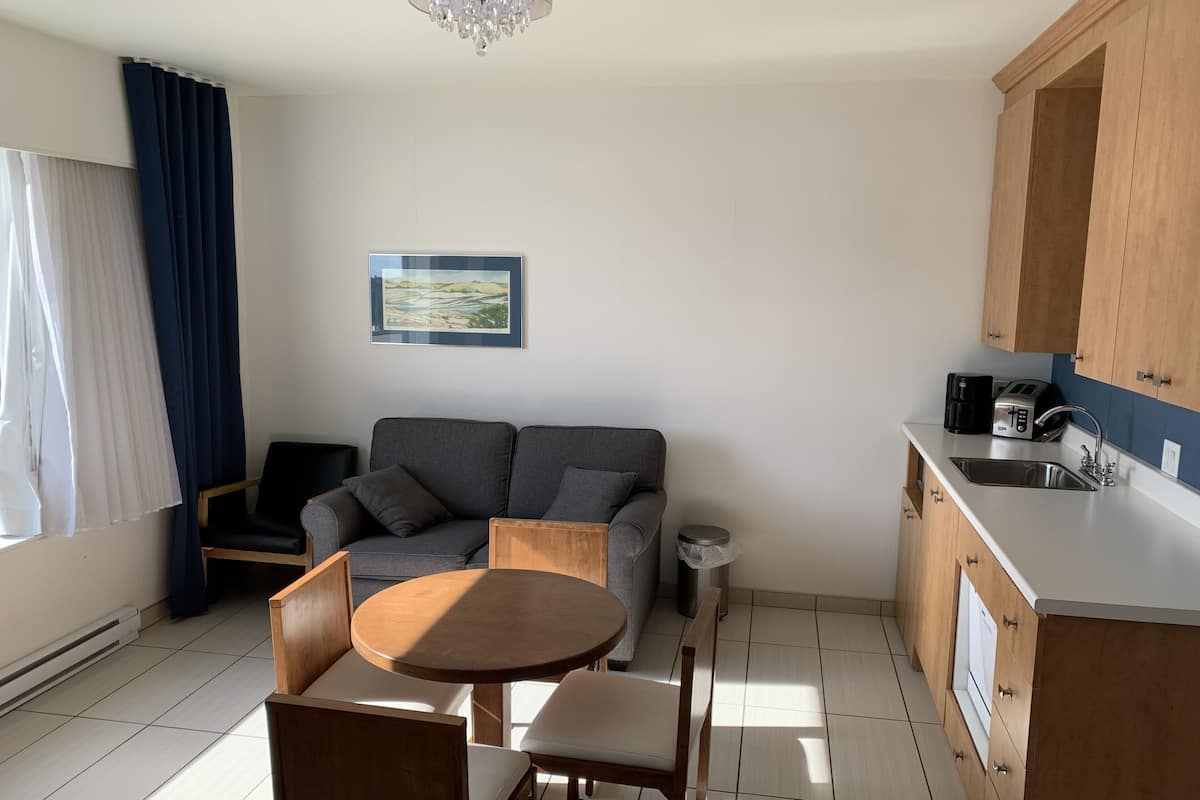 A compact living space with a sofa, a round wooden table, and a kitchenette.