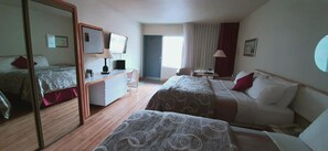 Two single beds with patterned bedding, a desk with a flat-screen TV, and a mirror.