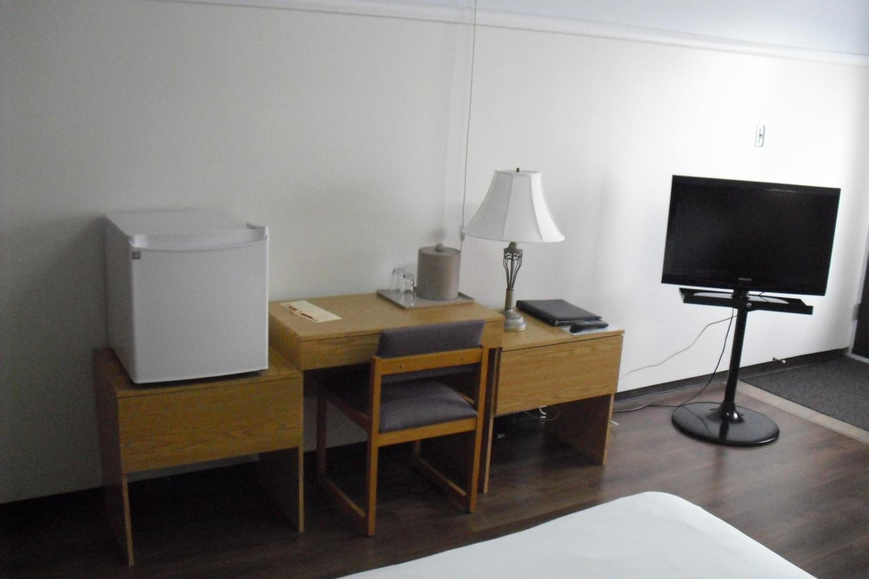 Une chambre d’hôtel comprenant un lit, un bureau avec une chaise, une lampe, une télévision et un réfrigérateur.