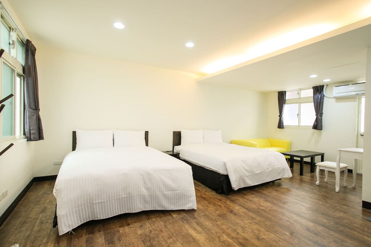 Una habitación de hotel con dos camas, un sofá amarillo, una mesita y una ventana con cortinas.