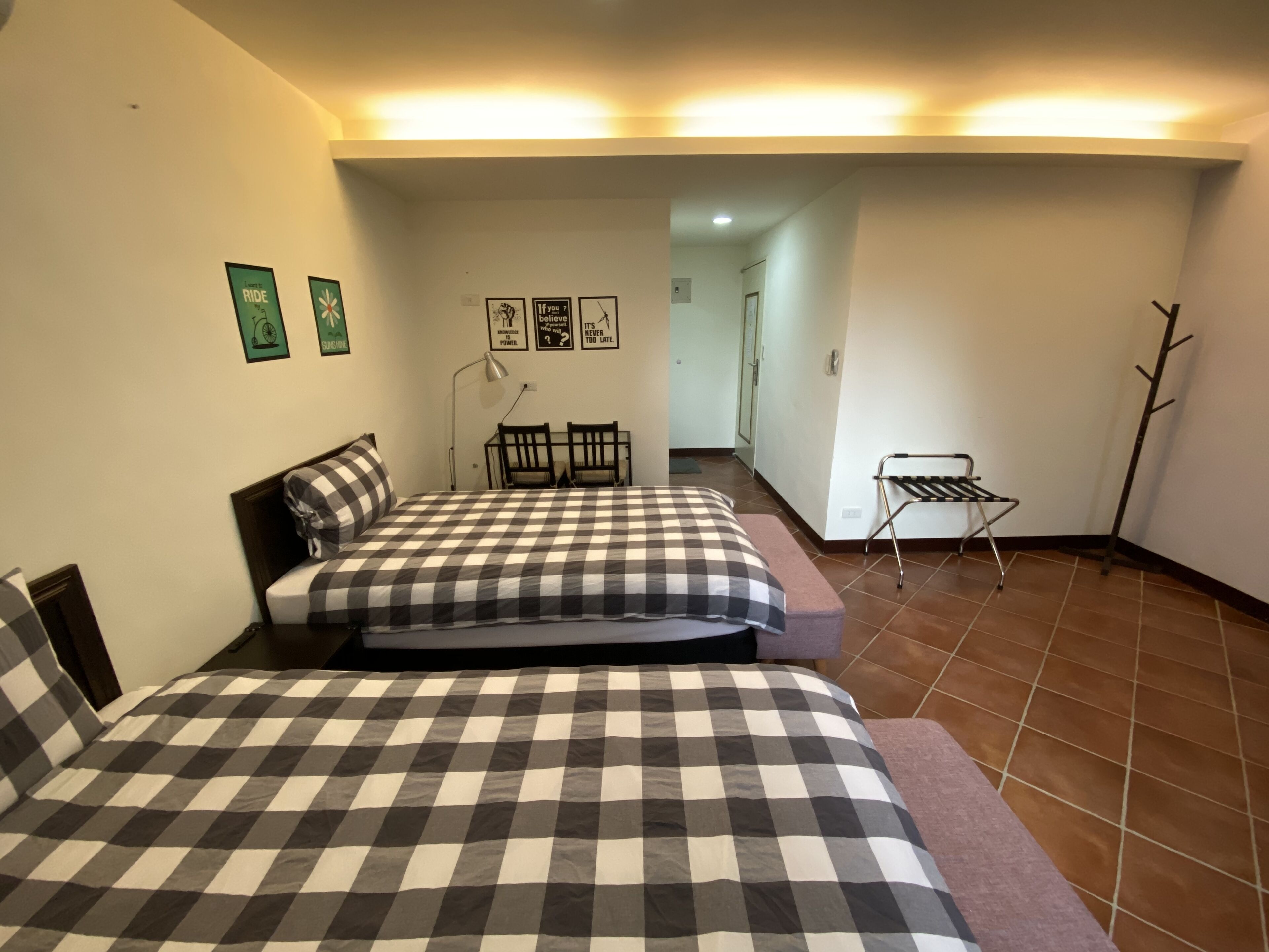 A bedroom with two beds, a chair, a small table, and a coat rack.