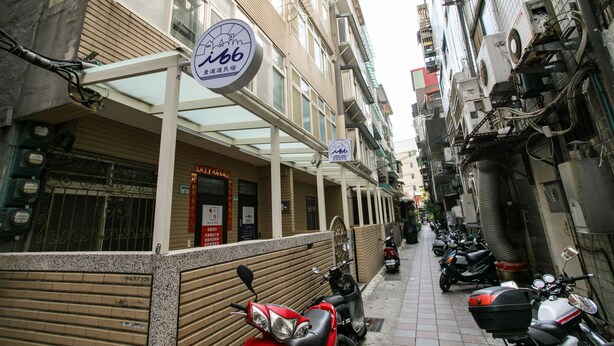 Uma rua estreita ladeada por edifícios, um letreiro de hotel e várias scooters estacionadas.