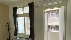 Quarto com mesa de vidro, duas cadeiras, janela com cortinas, ar condicionado e porta para o exterior.