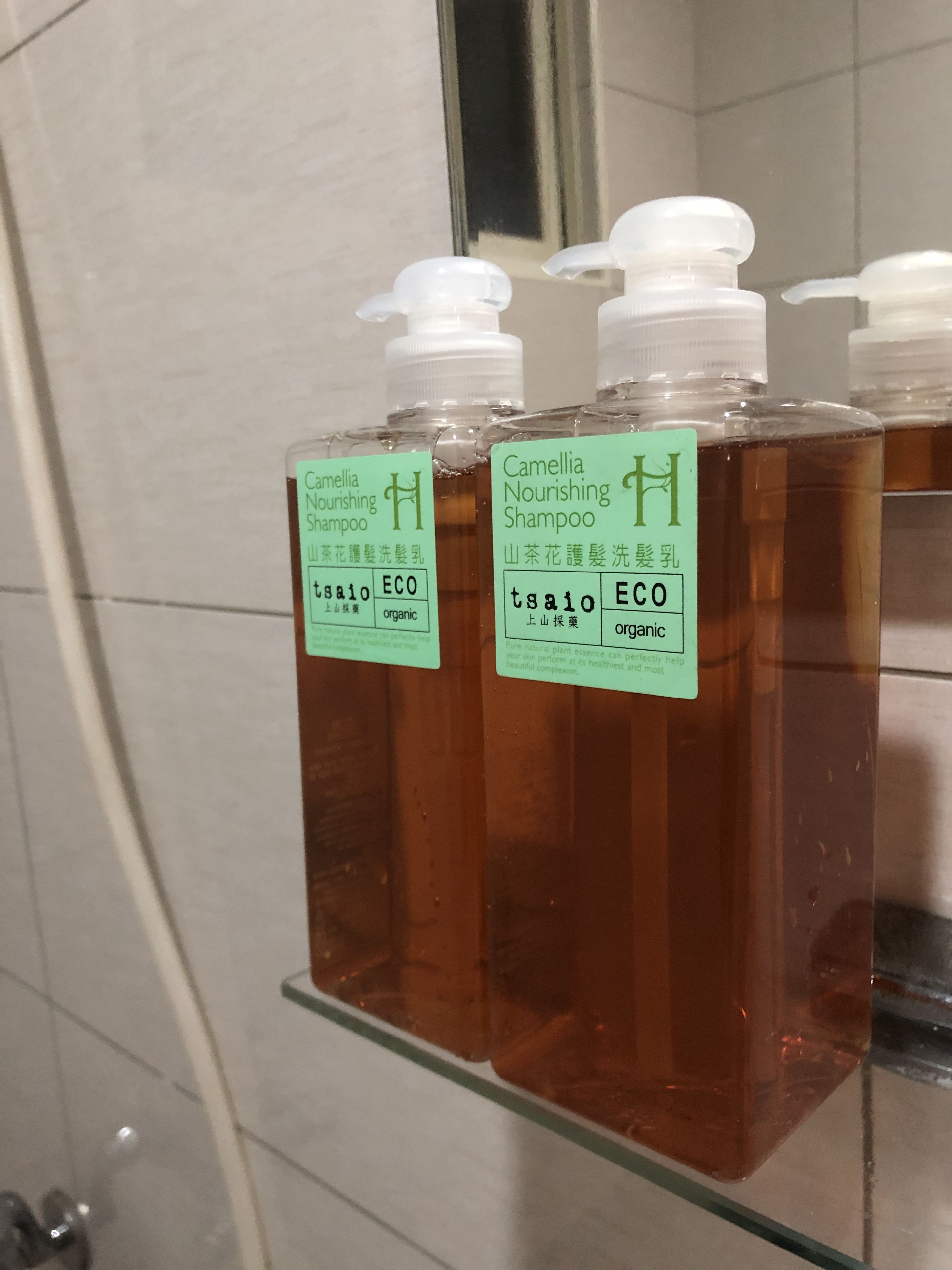 Bottles of Camellia Nourishing Shampoo on a glass shelf in a bathroom.