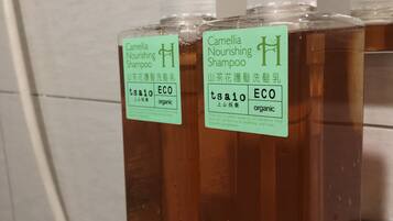 Bottles of Camellia Nourishing Shampoo on a glass shelf in a bathroom.