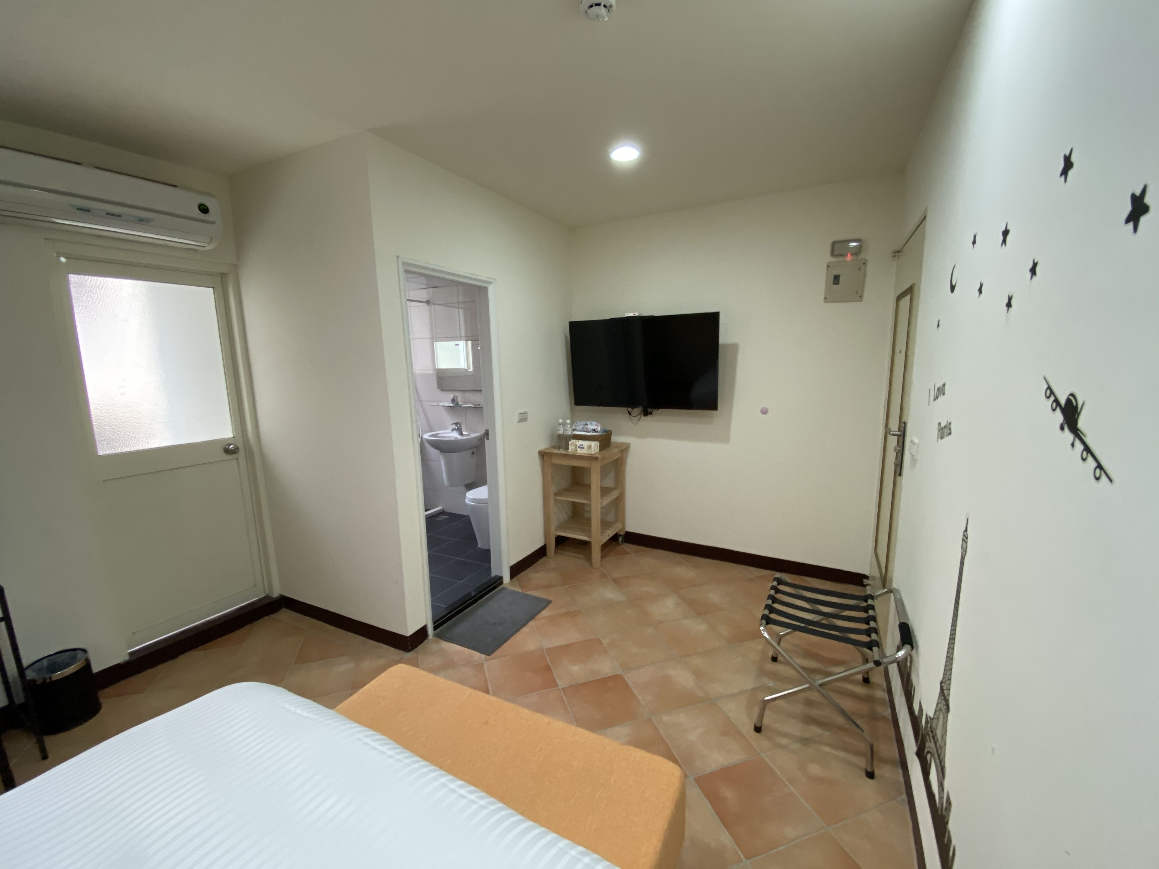 Une petite chambre propre, avec un lit, une télévision et une fenêtre.