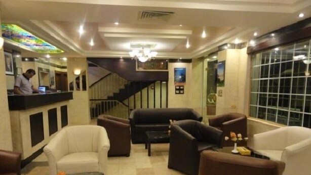 A lobby with a reception desk, seating area, staircase, and a large window. - Golden Palace Hotel Apartments (Amman)