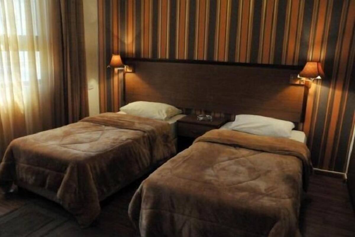 A hotel room with two single beds, striped wallpaper, and bedside lamps.