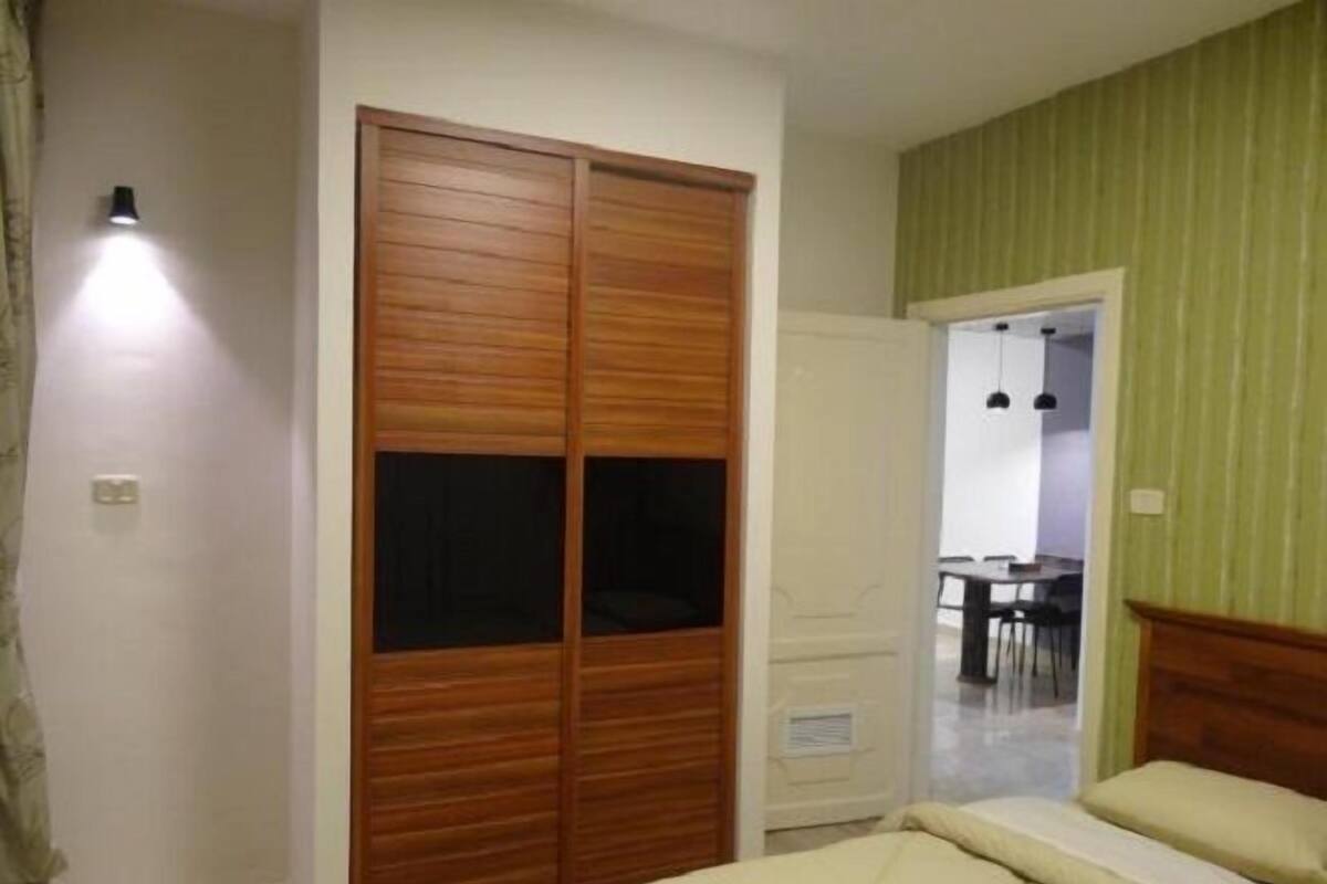 A bedroom with a wooden wardrobe, a bed, and a green-striped wall.