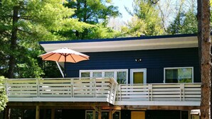 A two-story building with a covered patio area, outdoor seating, and a yellow door. - Quaint, Clean & Updated Cottage- Steps From The Beach. (Port Franks)