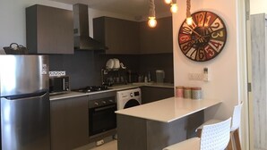 A modern kitchen with a central island, stainless steel appliances, and a unique wall clock.