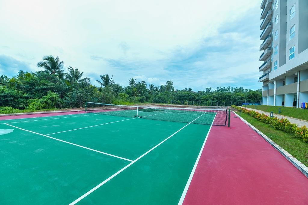 A tennis court with a net, surrounded by greenery and a building.