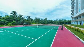 A tennis court with a net, surrounded by greenery and a building.
