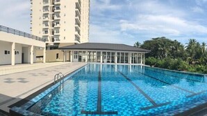 A swimming pool with a tiled deck, surrounded by a building with balconies and a covered area.