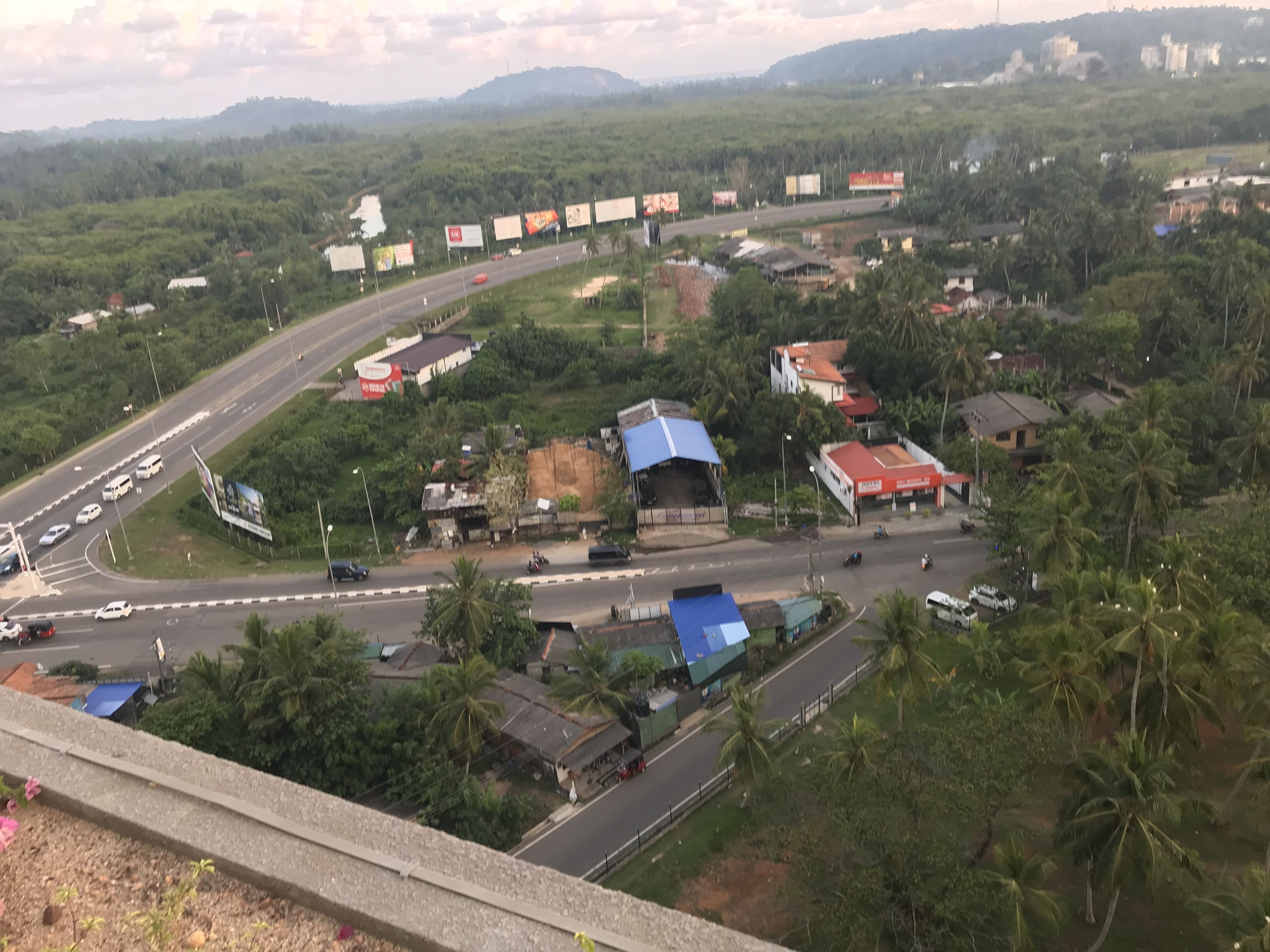 Carretera con varios carriles y vehículos, rodeada de vegetación y edificios con tejados rojos.