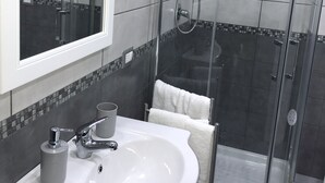 Un baño con ducha de vidrio, un lavamanos con espejo y pared de azulejos.