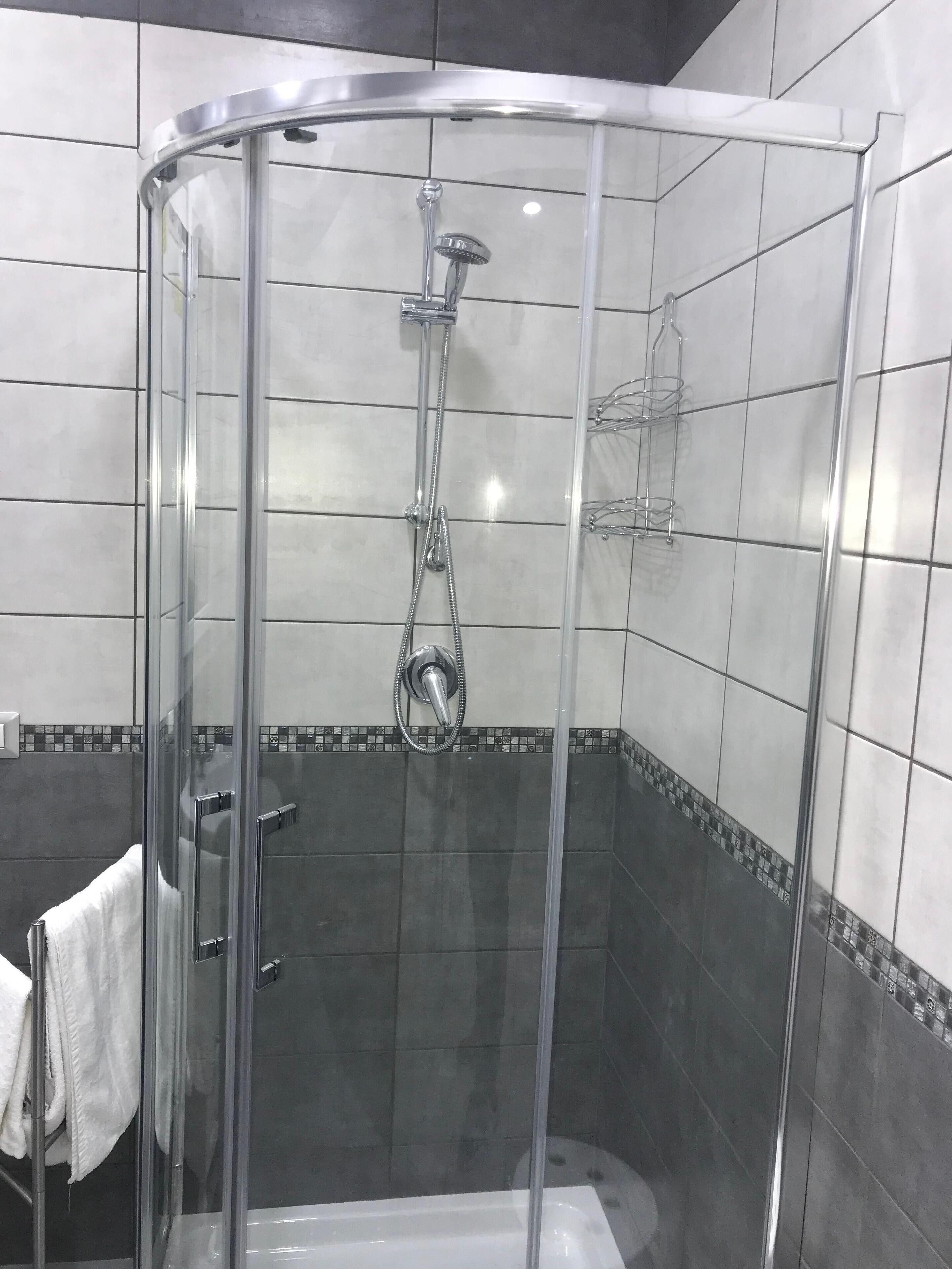 A glass-enclosed shower stall with a handheld showerhead, a glass door, and a tiled shower area.