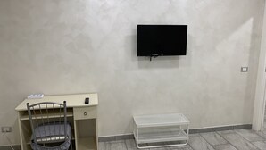 Una habitación con escritorio, silla, televisión y unidad de almacenamiento.