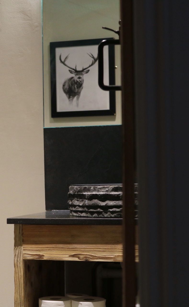 Un ciervo montado en la pared, un banco de madera y una pequeña mesa con un objeto estampado.