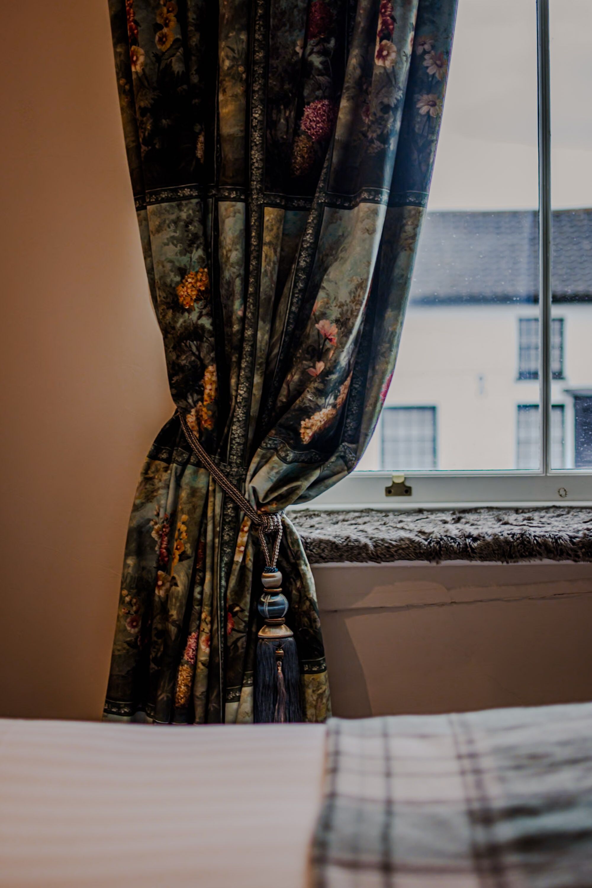 A window with floral curtains tied back, revealing a building outside.