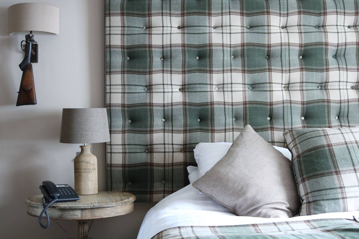 A bedroom with a plaid headboard, a bedside lamp, a telephone, and a decorative bottle.