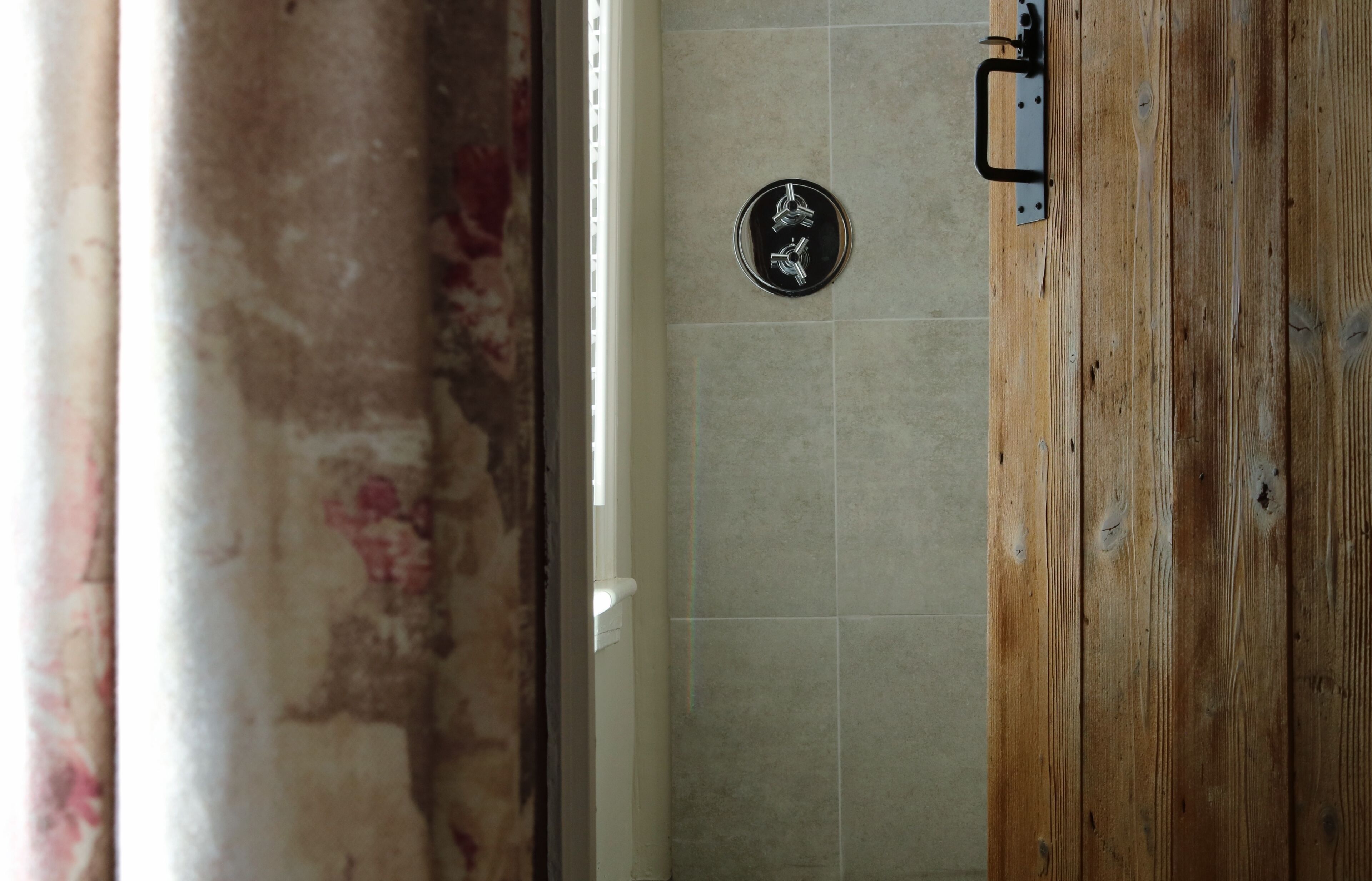 A bathroom with a wooden door, tiled walls, and a visible shower control panel.